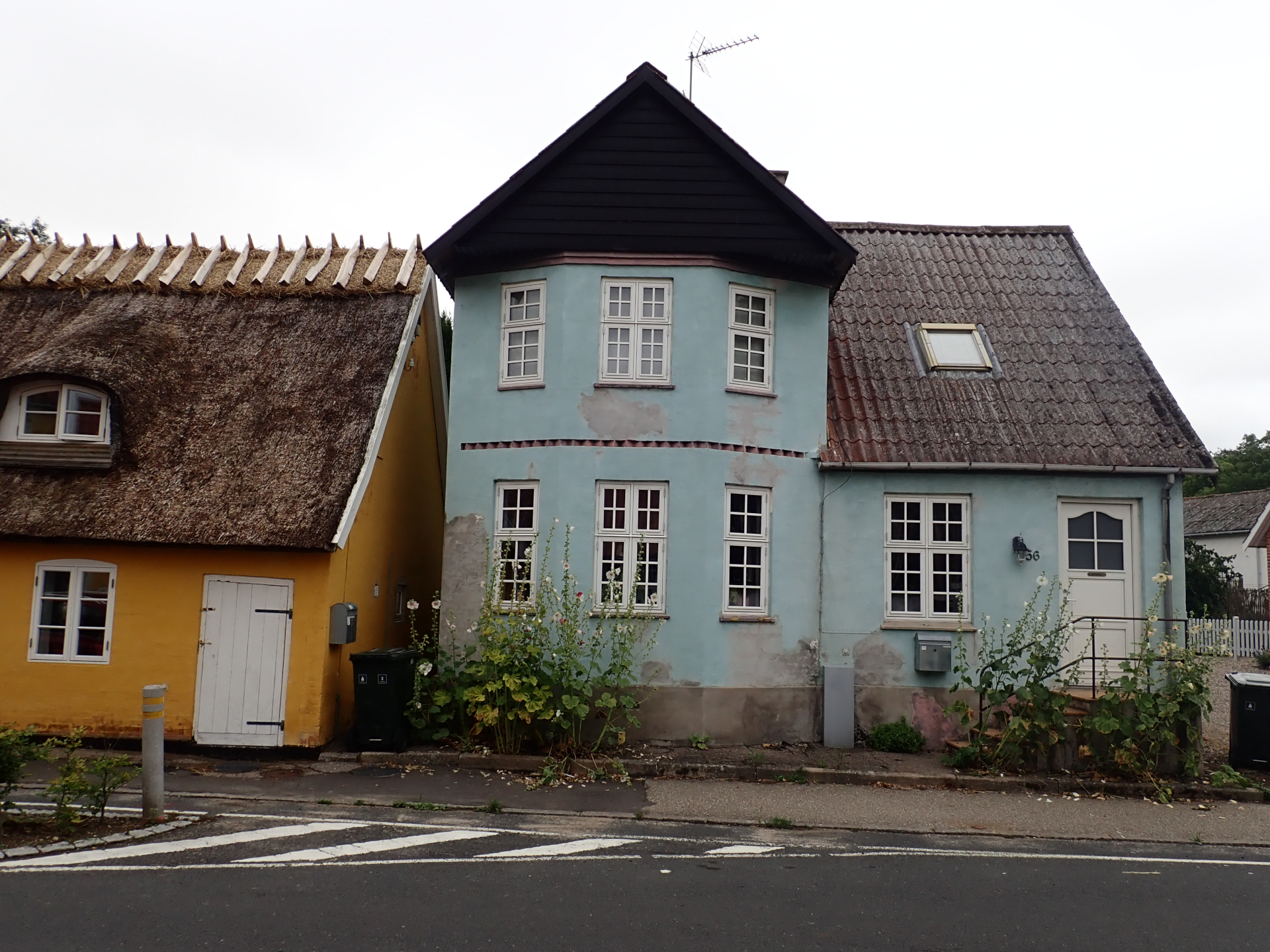 Two traditional Danish houses. The yellow one on the left has a grass rooftop; the light blue one on the right has a very triangular roof and flowers in front of it