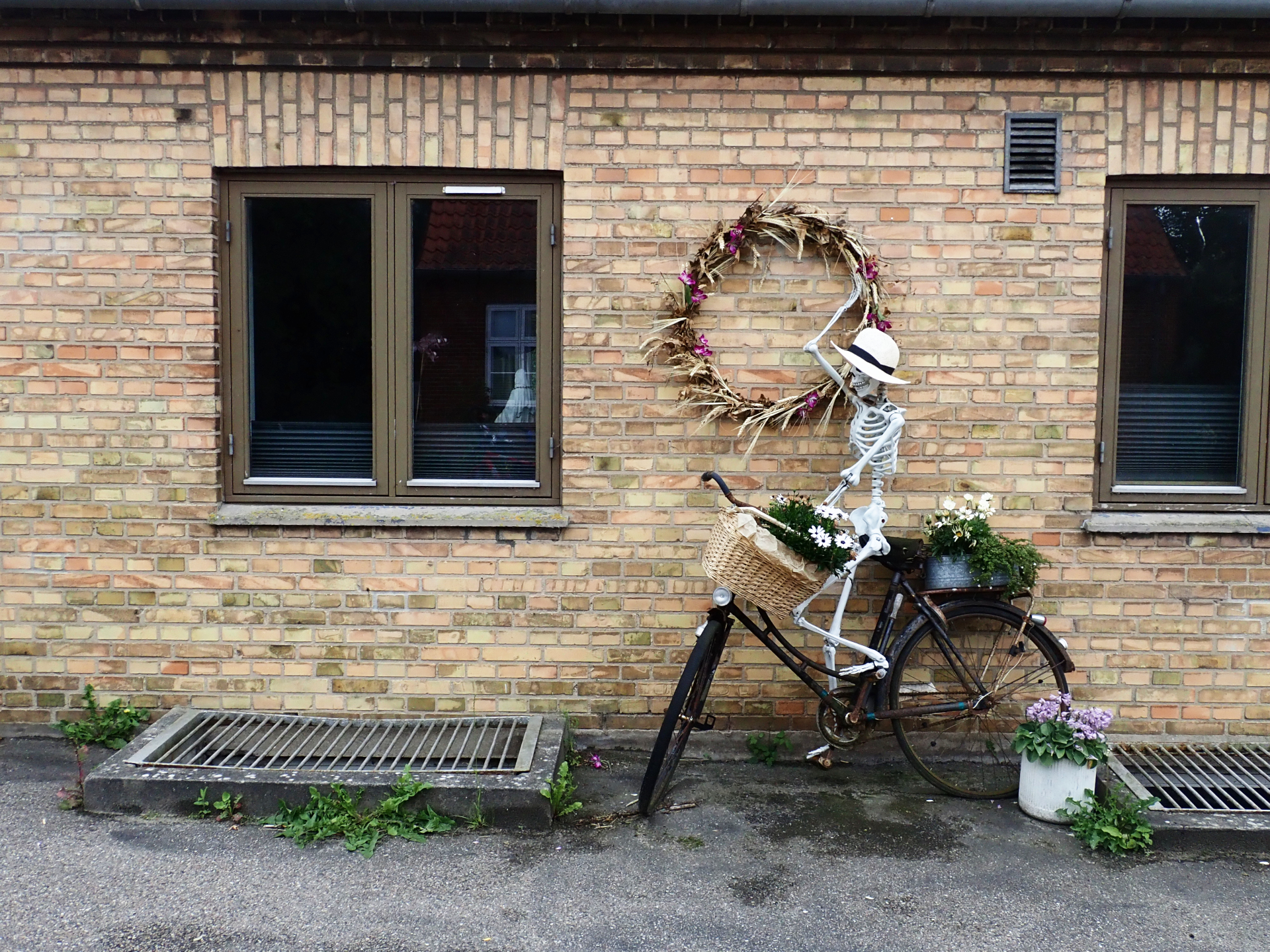 A skeleton with a hat riding a bike in front of a house.