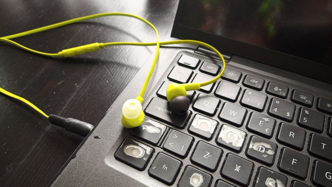 A pair of beaten up wired earbuds with a heavily taped jack plugged into an even more beaten up laptop
